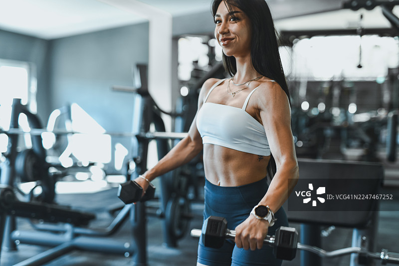 身着运动服的女性在健身房使用哑铃训练，在现代化的健身空间展现力量与健康图片素材