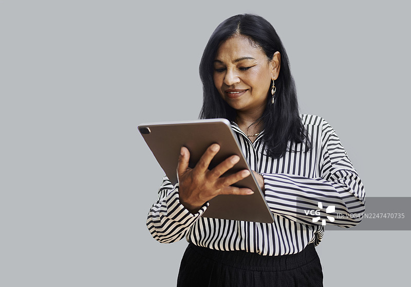 中年职业女性在影棚灯光下使用平板电脑，背景为灰色图片素材