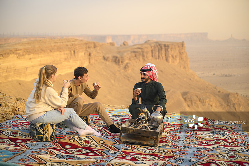 当地沙特导游与游客在世界尽头旅行目的地围坐在篝火旁，一同享用咖啡图片素材