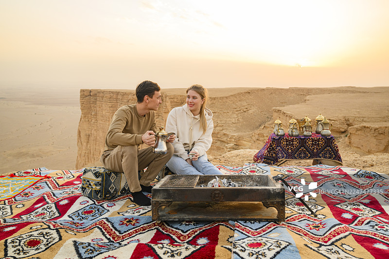 年轻的旅行者们在世界尽头的日落时分围着篝火一同享用咖啡图片素材