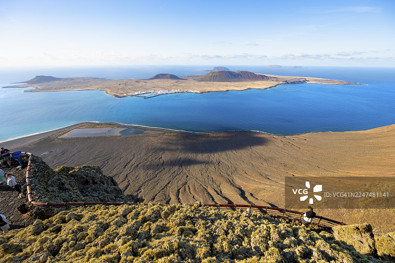 傍晚时分,从艺术家塞萨尔·曼里克设计的里约观景点(Mirador del Río)俯瞰拉格拉西奥萨岛,岛上有火山坑,观景台上还有游客,这里位于西班牙加那利群岛的兰萨罗特岛。图片素材