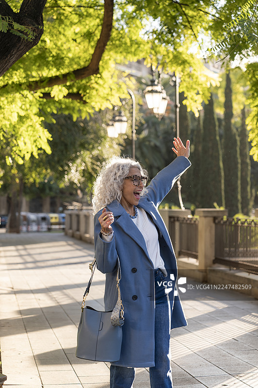 一位成熟的女士在城市街道上挥手图片素材