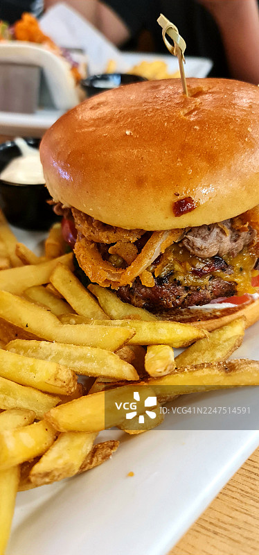 白色盘子上特写诱人的汉堡，配有酥脆的洋葱圈和金黄色的炸薯条图片素材