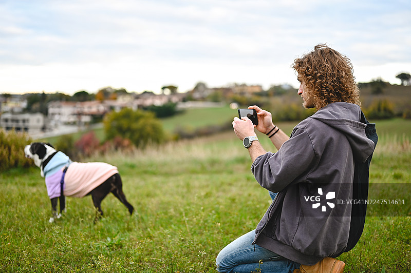 年轻男子在户外用智能手机给宠物狗拍照图片素材