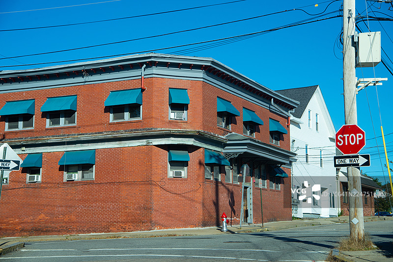 蓝顶旧砖砌建筑位于街角，有停车标志和电线，天空湛蓝，位于美国西沃里克图片素材