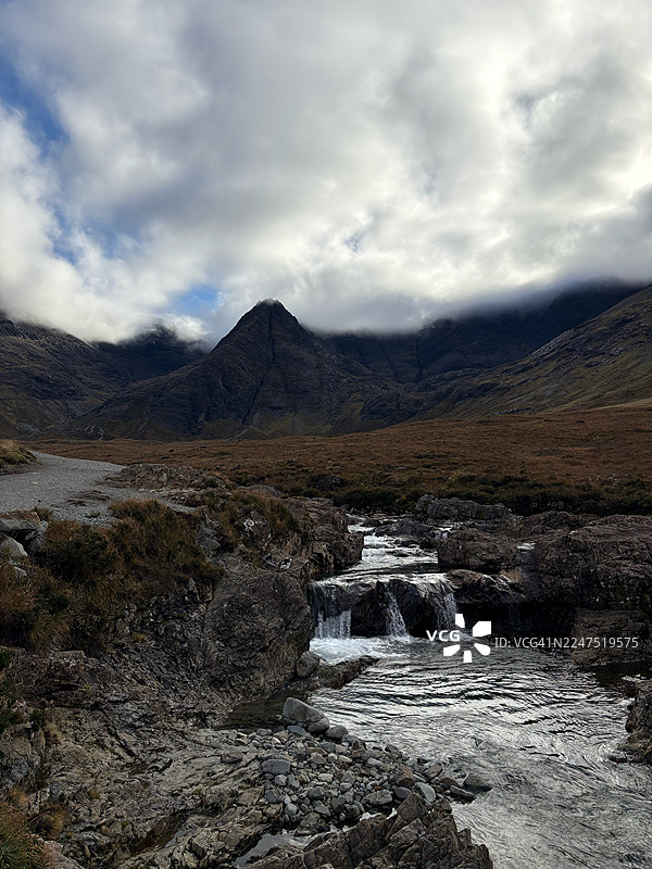 英国史密斯顿，溪流穿过岩石地形，远眺群山和多云的天空，仙境般的景色图片素材