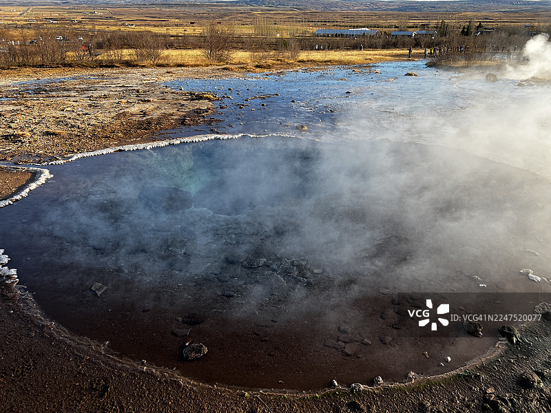 俯瞰冒着热气的温泉，背景是广阔的自然风光，展现了地热活动和自然之美图片素材