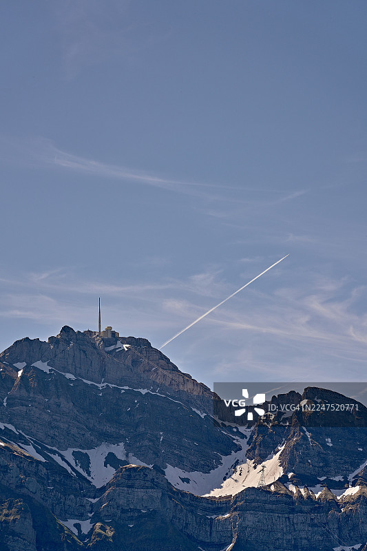 蓝天白云下，雪山壮丽，一道飞机尾迹划破天际。图片素材