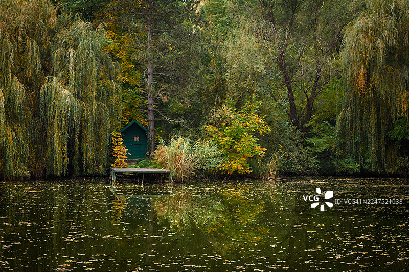 宁静湖泊边上的绿色小屋，带有木制码头，周围环绕着茂密的秋季树木图片素材