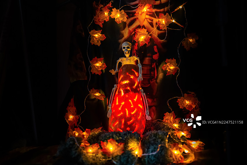 黑暗房间里，万圣节的幽灵装饰，有骷髅、发光的南瓜灯和秋叶串灯图片素材
