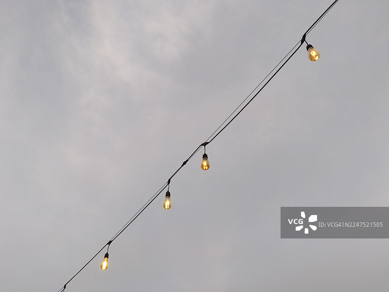 灯串的灯泡在多云的天空中点亮并垂挂着图片素材