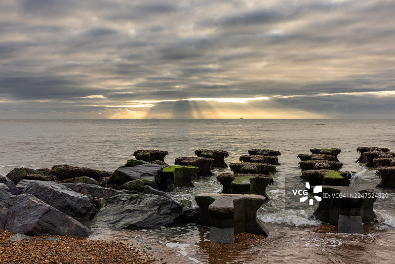 日落时分，戏剧性的天空映衬着海景，海边有岩石海岸和防波堤，英国，萨福克郡东部，费利克斯托图片素材