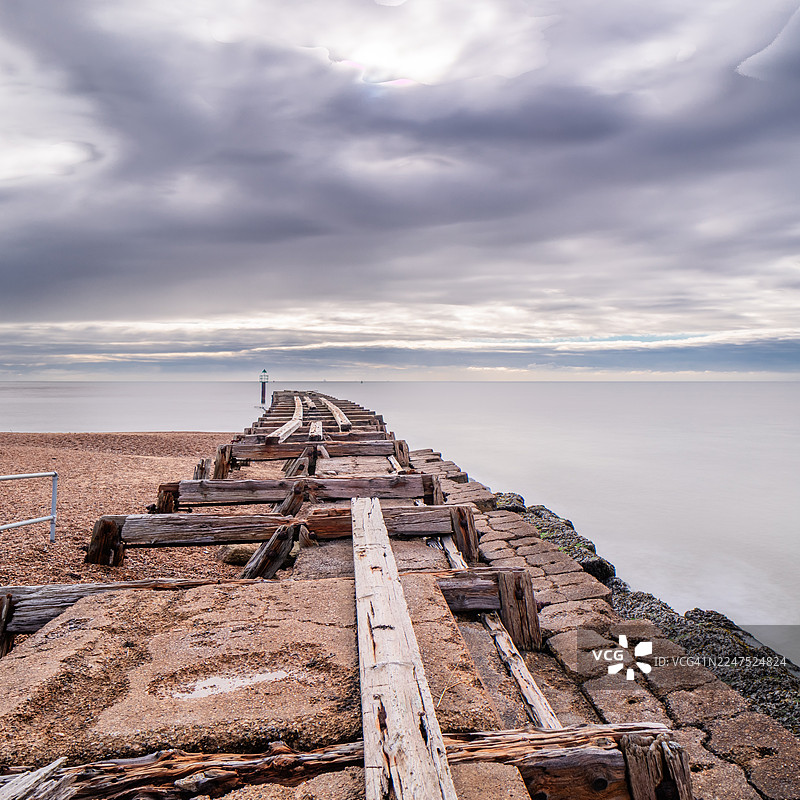一条古老的木制码头延伸入平静的海面，上方是戏剧性的多云天空图片素材