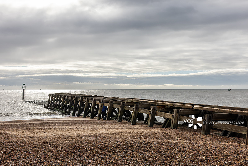 木制码头延伸入海，海面上方是戏剧性的多云天空，尽头是小灯塔图片素材