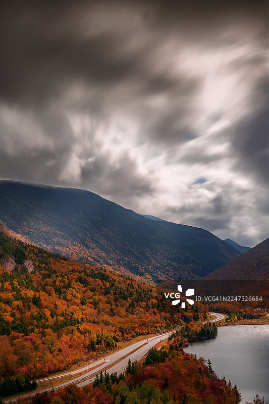 秋日里，山峦环抱的湖泊旁，蜿蜒的道路和秋叶在戏剧性的天空下构成一幅美景，位于美国康威的艾蔻湖。图片素材