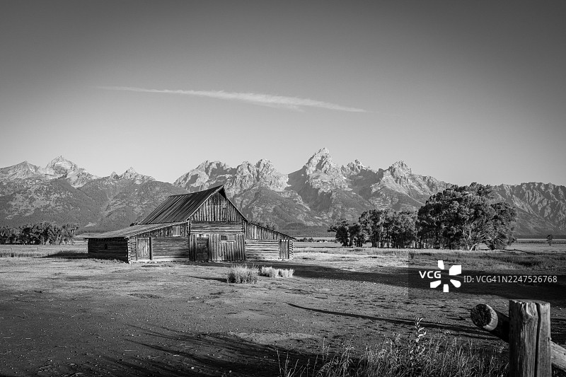 美国杰克逊，广阔田野里的质朴谷仓，背景是晴朗天空下的雄伟山脉，黑白。图片素材