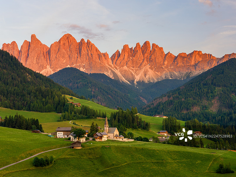 郁郁葱葱的山谷中风景如画的村庄，背景是夕阳下壮丽的白云岩山脉，富内斯，意大利，富内斯公交车站图片素材