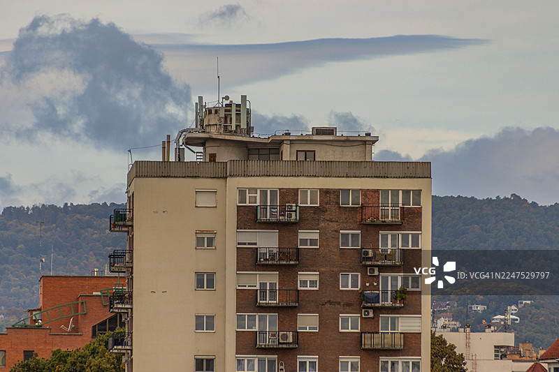 多层建筑带有阳台，背景是多云的天空和山丘，展示了布达佩斯，匈牙利的城市建筑图片素材