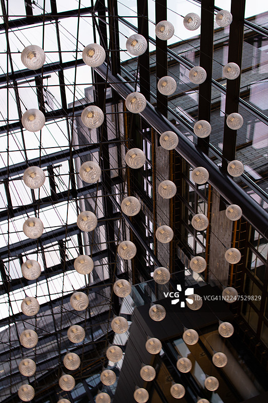 现代玻璃球形灯具悬挂在高高的天花板上，位于一栋现代建筑的室内，形成抽象图案。图片素材