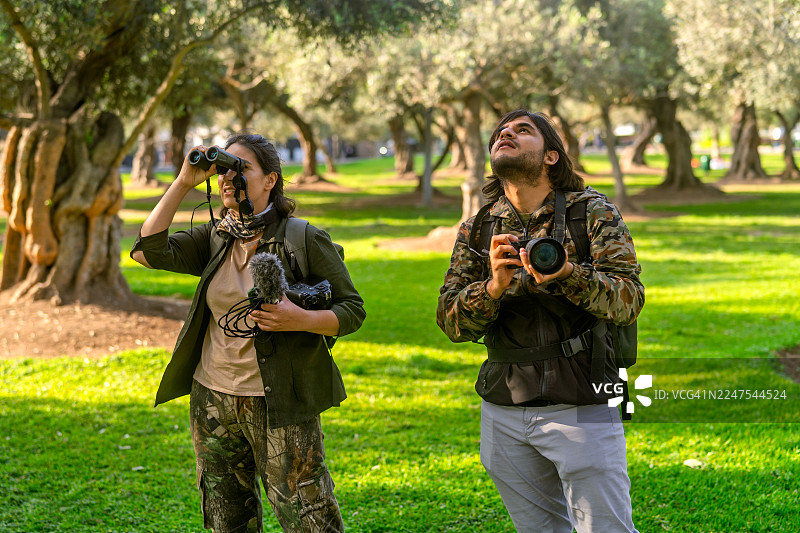 一对情侣在城市公园里用望远镜和相机观鸟图片素材
