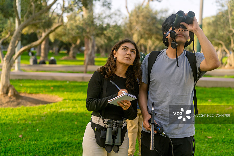 年轻的观鸟者在公园里观察鸟类并记录数据图片素材