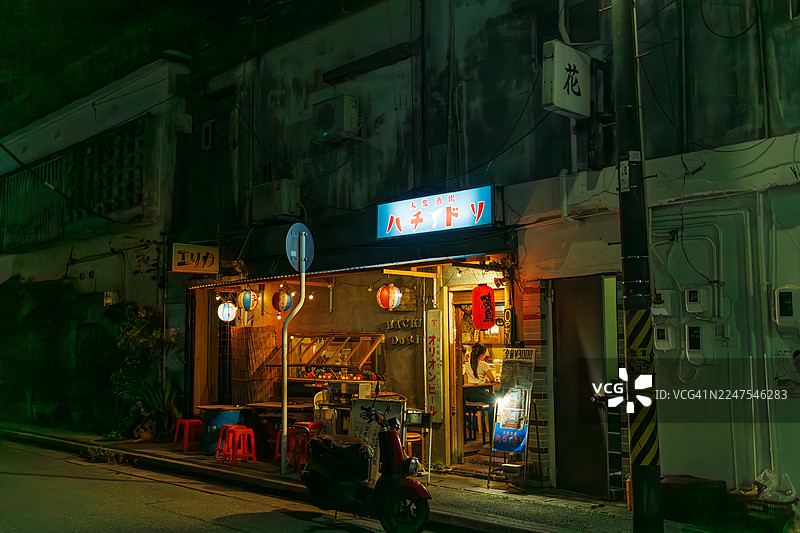 日式居酒屋的外景。开放式露台吧台和老式踏板摩托车展示。游客进入店内。偶尔有出租车经过。图片素材