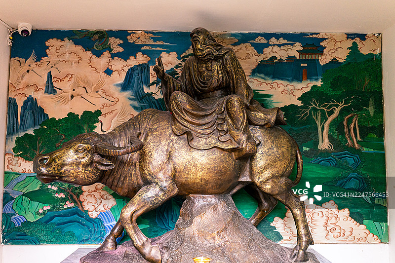 老子骑着水牛的青铜雕像，展示了道教和中国文化的重要象征，背景是中国古典山水壁画图片素材