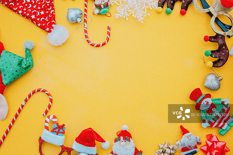 芥末色背景上的圣诞相框，边缘装饰着节日装饰品，中心留有白色空白，还有圣诞老人玩偶、拐杖糖道具、绿色闪光圣诞树太阳镜、驯鹿角头饰、小饰品，构成一个俏皮的节日边框，色彩明亮图片素材