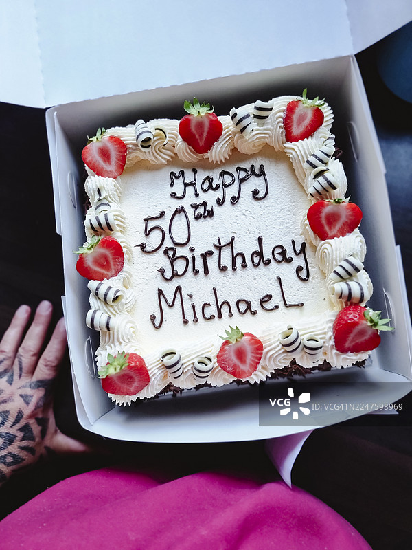 50岁生日庆典蛋糕装在盒子里。打开的蛋糕盒和旁边站着的人的俯视图。图片素材