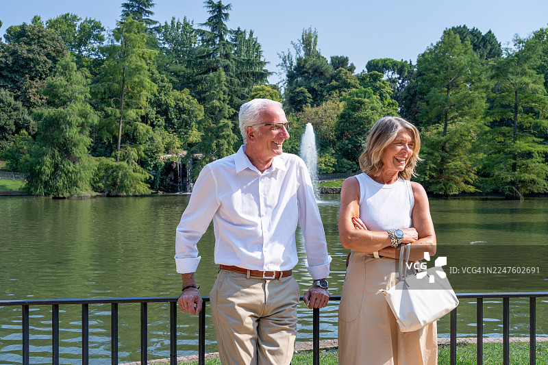 一对年长夫妇在西班牙马德里丽池公园湖边享受浪漫的夏日假期，他们微笑着、欢笑着，体验着长久关系的喜悦。图片素材