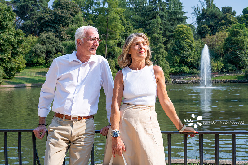 一对成熟的夫妇在马德里 retiro 公园湖边放松，享受退休生活和浪漫约会，这是他们欧洲假期的一部分。图片素材