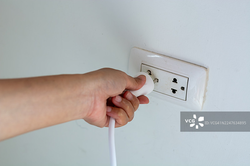 手持电源插头插入干净水泥墙壁的插座图片素材