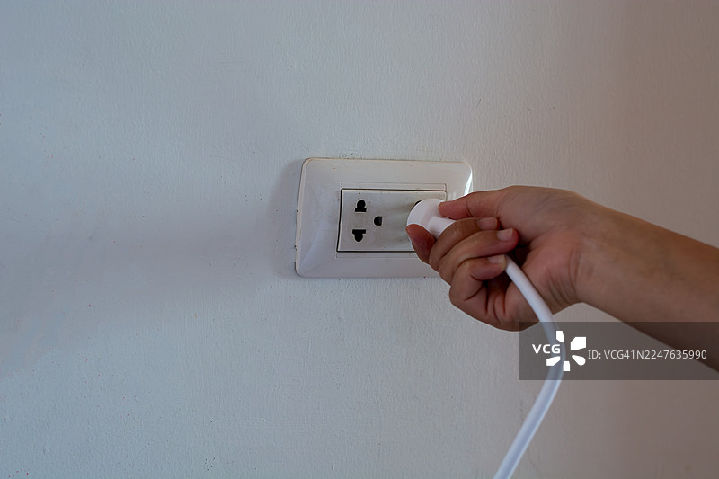手持电源插头插入干净水泥墙壁的电源插座图片素材