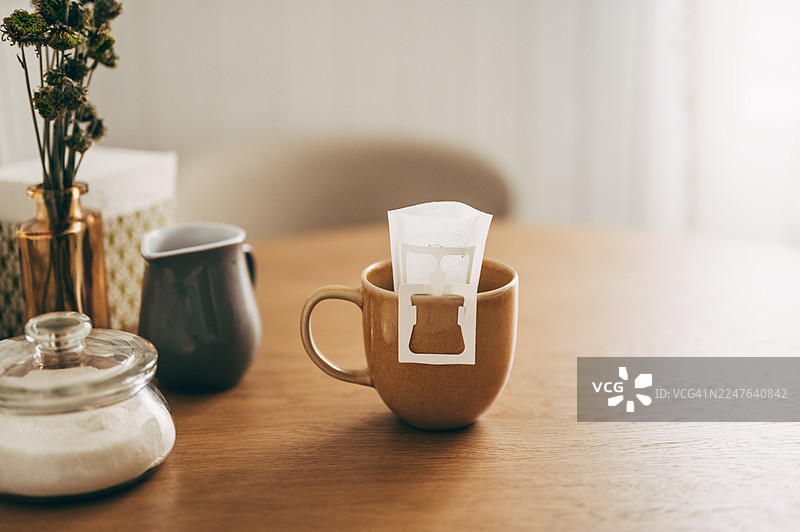 特写：从水壶中向木桌上的杯子倒入热水，杯中有滴滤咖啡包图片素材