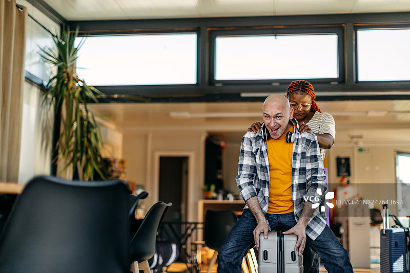 多民族情侣在咖啡馆等待交通工具，准备去度假，坐在行李箱上互相嬉闹图片素材