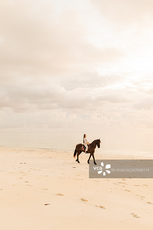 一位女士在日落时分，于桑给巴尔海边的广阔海岸线上骑马而行图片素材