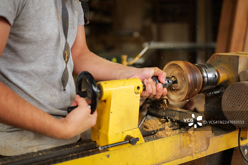 木匠在繁忙的车间里熟练地用刨床加工木材，塑造一件独特的家具，锯末四处飞扬，弥漫在空气中。图片素材