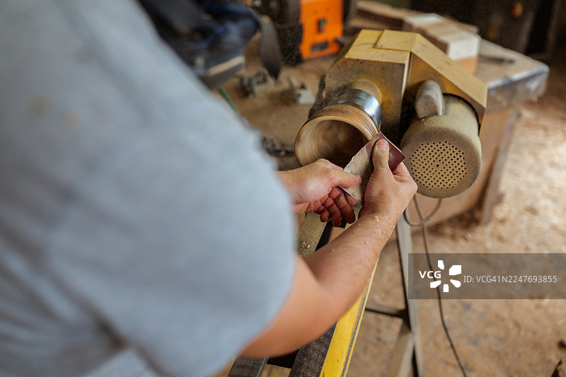 木匠在车床上用砂纸细致地打磨一个木碗，在弥漫着新鲜木材香气的质朴工作室里制作一件精美的纯手工艺术品图片素材