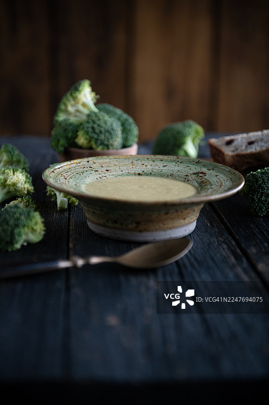 深色乡村风格的桌子上，陶瓷碗里盛着西兰花奶油浓汤图片素材
