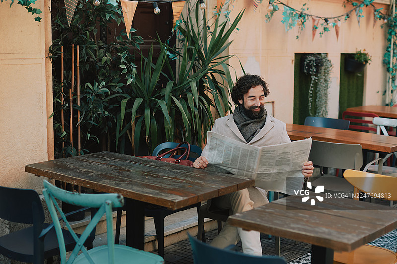英俊的成年男子在户外咖啡馆里，在植物和节日装饰中看报纸图片素材