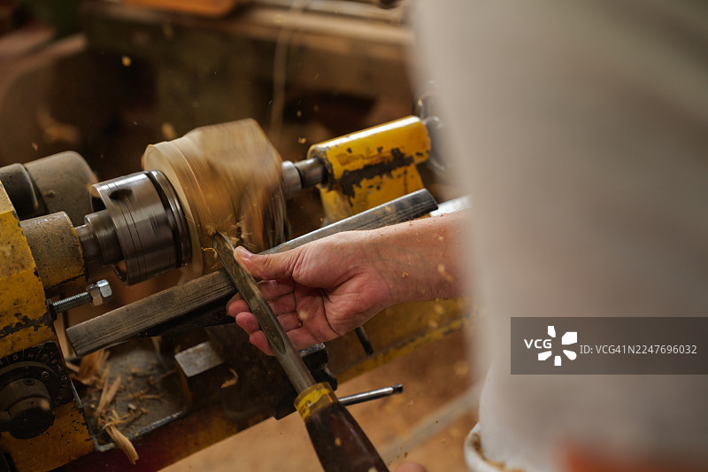 木匠的双手娴熟地在车床上加工木材，塑造着原始的木料，车间里弥漫着木屑飞舞的景象，彰显了木工的艺术性图片素材