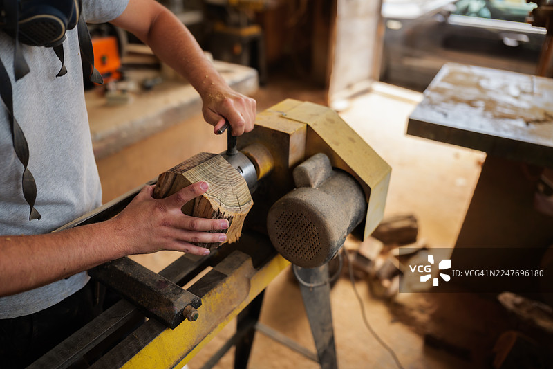 一位木匠戴着防护口罩，在尘土飞扬的旧工作室里熟练地操作车床加工木材，一丝不苟地精心制作一件独特的纯手工家具图片素材