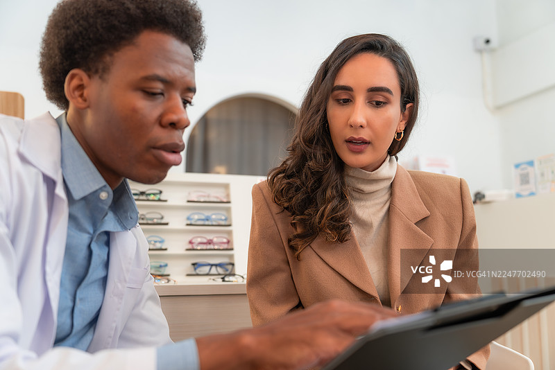验光师在零售眼科检查咨询中，利用数字平板技术为多元化患者提供眼镜选择建议。图片素材