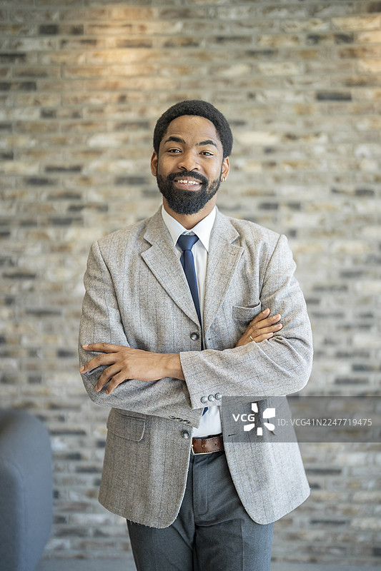 自信的商人，双臂交叉，在现代办公室里微笑图片素材