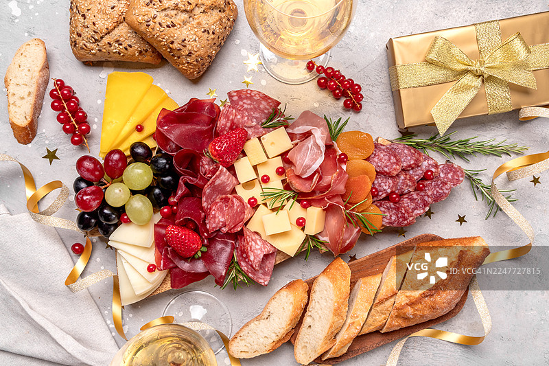 圣诞树造型的熟食拼盘，包含意大利熏火腿、火腿、萨拉米香肠、奶酪和格里西尼面包棒，搭配着白葡萄酒、普罗塞克或香槟，以及节日装饰。图片素材