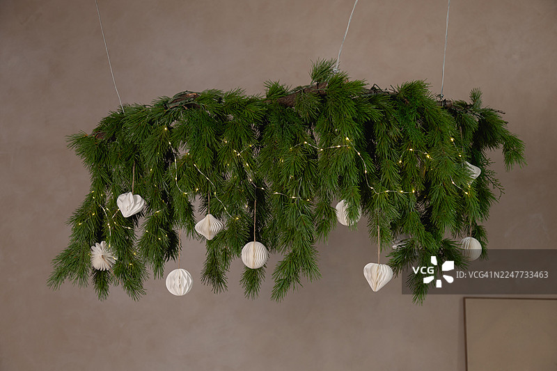 天花板上悬挂着郁郁葱葱的常绿树枝，装饰着白色纸质饰品和一串闪烁的仙女灯。图片素材