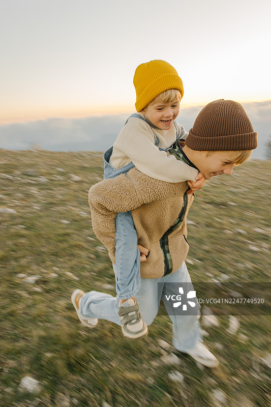 夕阳下，两个孩子在户外快乐地玩耍，一个背着另一个图片素材