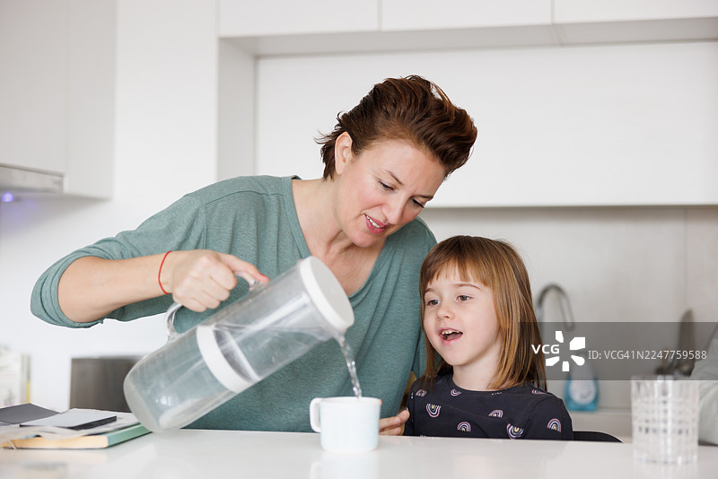 中年女性在厨房操作台前为小女儿倒水图片素材