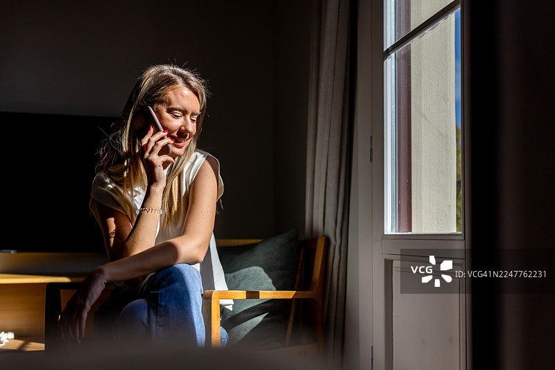 阳光透过窗户洒进客厅，女子在窗边接听电话，享受着惬意与愉悦的时光。图片素材