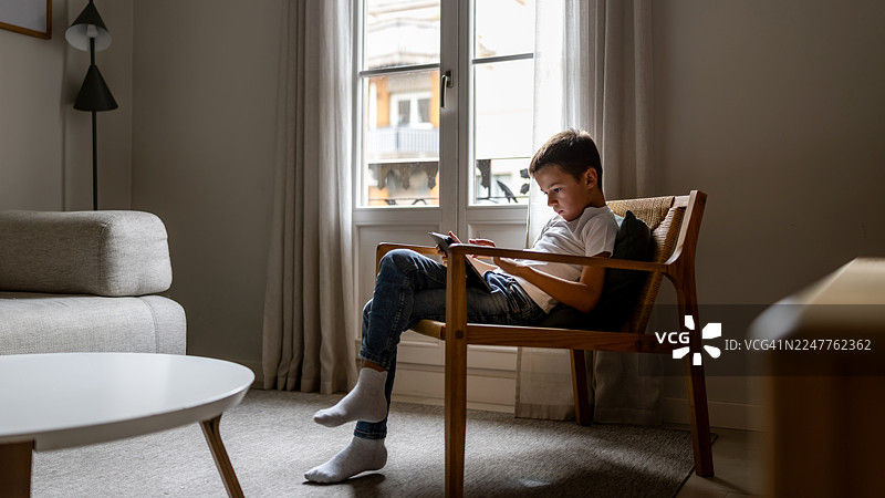 男孩坐在舒适的扶手椅上阅读，温馨的客厅一刻图片素材